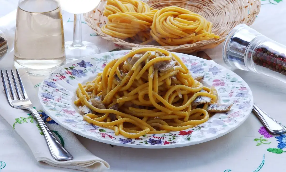 Un piatto di bigoli in salsa, con pasta fresca, acciughe e cipolla, pronto per essere gustato.
