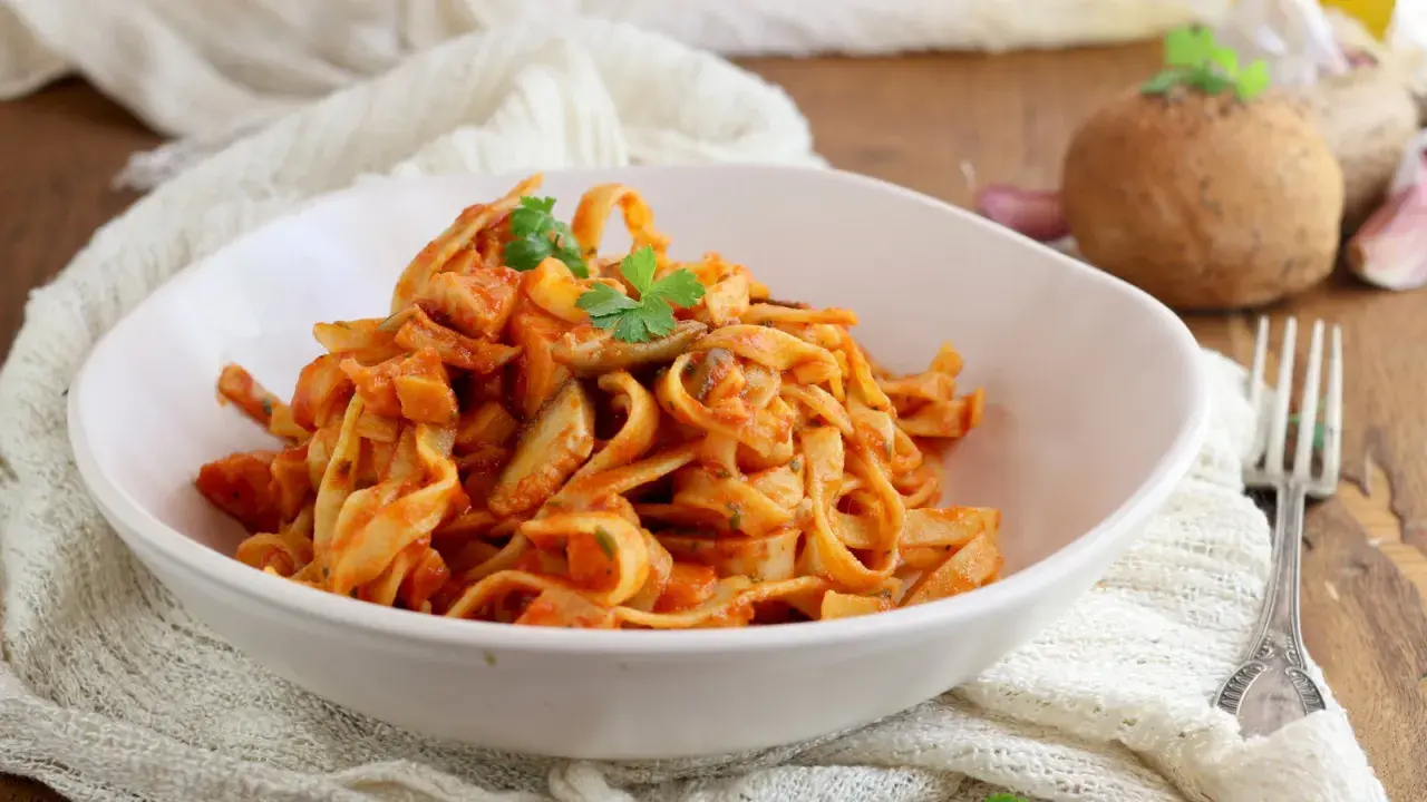 Un piatto invitante di tagliatelle ai funghi, condite con una ricca salsa al pomodoro e guarnite con prezzemolo fresco.