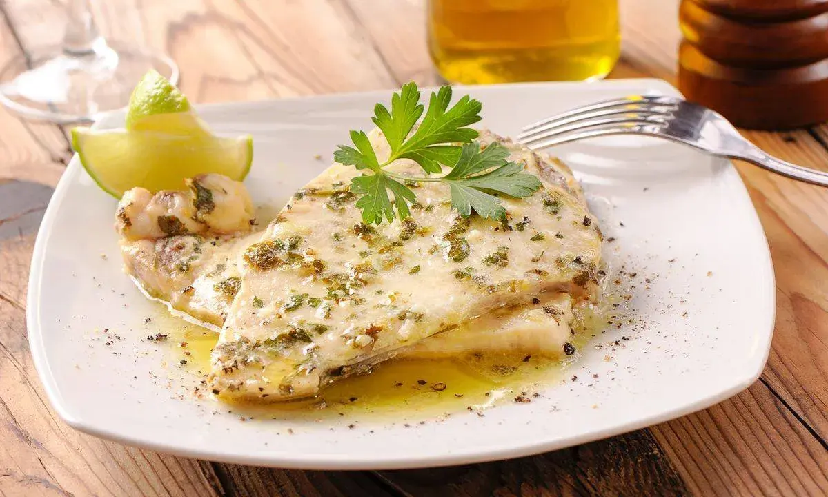 Delizioso pesce spada al forno, condito con erbe aromatiche e servito con spicchi di lime e prezzemolo fresco.