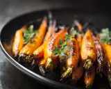 Carote caramellate e dorate, cotte in friggitrice ad aria, guarnite con erbe aromatiche fresche su un piatto scuro.