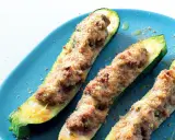 Tre zucchine ripiene, dorate e gratinate, servite su un piatto blu. Un piatto invitante e saporito.