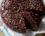 A rich, moist chocolate cake topped with chocolate chips, with a slice cut out to show its texture.