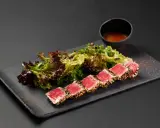 Tataki di tonno scottato, servito con insalata fresca e una ciotolina di salsa.