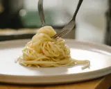 Spaghetti al limone serviti su un piatto bianco, con due forchette che raccolgono la pasta.
