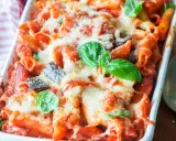 Penne al forno con melanzane, pomodoro e abbondante formaggio filante, guarnite con basilico fresco.