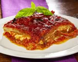 Una fetta di parmigiana di melanzane napoletana, ricca e saporita, guarnita con basilico fresco.