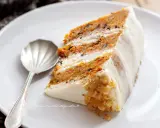 Una fetta di torta di carote e yogurt, soffice e profumata, con glassa bianca e noci tritate.
