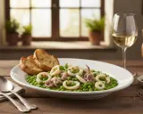 Piatto di seppie con piselli, accompagnato da pane tostato e un bicchiere di vino bianco.