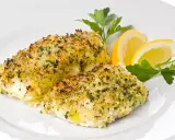 Delizioso merluzzo al forno con crosta croccante di erbe e pangrattato, guarnito con spicchi di limone e prezzemolo fresco.