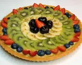 A fruit tart with kiwi, banana, strawberries, blueberries, and cherries on a custard filling.