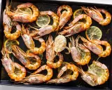 Gamberoni al forno dorati e succulenti, conditi con erbe aromatiche e spicchi di limone, pronti per essere gustati.