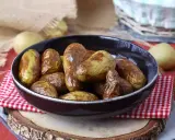Patate novelle dorate e croccanti, appena sfornate dalla friggitrice ad aria, servite in una ciotola scura su un tagliere di legno.
