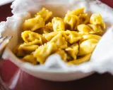 Un primo piatto invitante: tanti ravioli del plin dorati, serviti in una ciotola bordata di bianco.