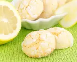 Biscotti al limone spolverati di zucchero a velo, accanto a fette di limone fresco su sfondo verde.