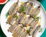 Piatto di alici al forno dorate e croccanti, guarnite con finocchietto fresco e un filo d'olio.