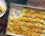 Fette di zucchine al forno con mozzarella filante, disposte in file ordinate in una teglia e su un piatto bianco.
