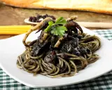 Un piatto invitante di spaghetti al nero di seppia, con tentacoli di calamaro e prezzemolo fresco, su una tovaglia a quadri verdi.