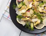 Un'insalata di carciofi crudi, con fette di limone, ravanelli e scaglie di parmigiano, guarnita con aneto fresco.