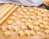 Piccoli gnocchi di ceci sparsi su un tagliere di legno, pronti per essere cotti.