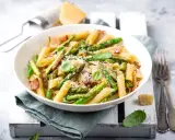 Piatto di pasta con asparagi e pancetta croccante, guarnito con basilico fresco e parmigiano grattugiato.