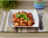 Un piatto di ravioli di carne conditi con sugo rosso e basilico fresco, pronti per essere gustati.