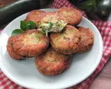 Piatto di polpette di zucchine e ricotta dorate e croccanti, guarnite con menta fresca.