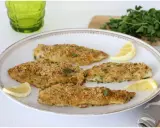 Four breaded fish fillets on a white plate with lemon wedges and parsley.