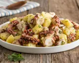 Delizioso polpo con patate, condito con prezzemolo fresco, servito in un piatto bianco su un tavolo di legno rustico.