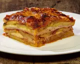 Una fetta di parmigiana di patate, stratificata con formaggio e salumi, servita su un piatto bianco.