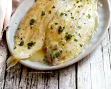 Sogliola alla mugnaia dorata e succulenta, cosparsa di prezzemolo fresco, servita su un piatto ovale.
