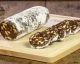 Un rotolo di salame al cioccolato, cosparso di zucchero a velo, affiancato da fette tagliate su un tagliere di legno.