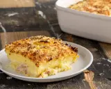Una fetta di sformato di patate dorato e croccante, con prosciutto e formaggio filante, servita su un piatto bianco.