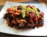 Un piatto di saporita caponata di melanzane, guarnita con foglie di basilico fresco.