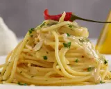 Spaghetti conditi con aglio, olio e peperoncino, guarniti con prezzemolo e un peperoncino rosso. Sullo sfondo, un bulbo d'aglio e una bottiglia d'olio.