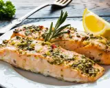 Delizioso salmone al forno con erbe aromatiche, aglio e peperoncino, guarnito con rosmarino e una fetta di limone.
