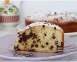 Una fetta di torta soffice con tante gocce di cioccolato, spolverata di zucchero a velo, su un piatto lilla con una forchetta.