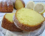 Fette di un soffice ciambellone al limone, spolverate di zucchero a velo, con spicchi di limone sullo sfondo.