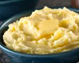 Una ciotola blu piena di soffice purea di patate, con una fetta di burro che si scioglie sopra.