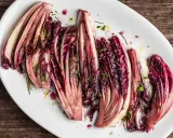 Radicchio al forno, tagliato a spicchi e condito con erbe aromatiche, servito su un piatto bianco.