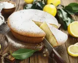 Torta al limone velocissima, spolverata di zucchero a velo, con una fetta tagliata e limoni freschi intorno.