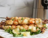 Spiedini di pesce croccanti, con gamberi e calamari impanati, serviti su un letto di insalata con spicchi di limone.