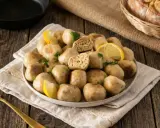 Piatto di polpette tonno e ricotta, guarnite con limone e prezzemolo, su un tavolo di legno rustico.