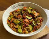 Insalata di lenticchie colorata con zucchine, carote e pomodori secchi, servita in una ciotola con la scritta "tutti a tavola".