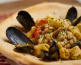 Un piatto invitante di pasta fagioli e cozze, con pomodorini e prezzemolo fresco, servito in una ciotola di pane croccante.