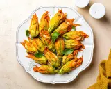 Fiori di zucca al forno ripieni, dorati e invitanti, disposti su un piatto bianco, con foglie di basilico fresco.