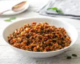 Un piatto invitante di lenticchie in umido, condite con pomodoro e cipolla, servite in una ciotola bianca su un tavolo di legno.