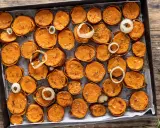 Fette di patate dolci al forno, dorate e condite con erbe aromatiche e sale, disposte su una teglia con anelli di cipolla.