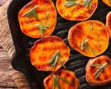 Fette di patate dolci grigliate in padella, condite con rosmarino e spezie, pronte per essere gustate.