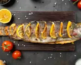 Un succulento pesce alla brace, guarnito con fette di limone e erbe aromatiche, pronto per essere gustato.