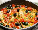 Pesce spada alla siciliana in padella con pomodorini, olive nere e capperi, guarnito con prezzemolo fresco.